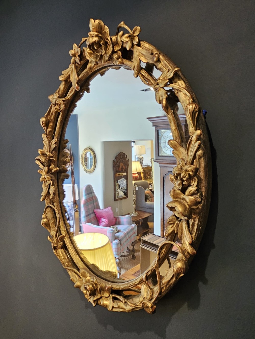 An oval Victorian giltwood wall mirror featuring a frame intricately carved with rose blossoms, foliage, and vine motifs. View VII