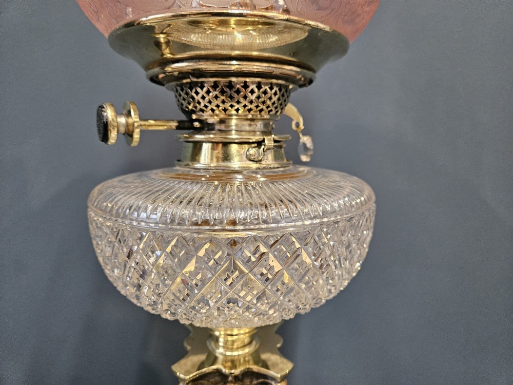 A Victorian oil lamp featuring a stepped brass base, fluted Corinthian column stem, cut crystal reservoir, etched pink glass shade, and clear glass chimney. View III
