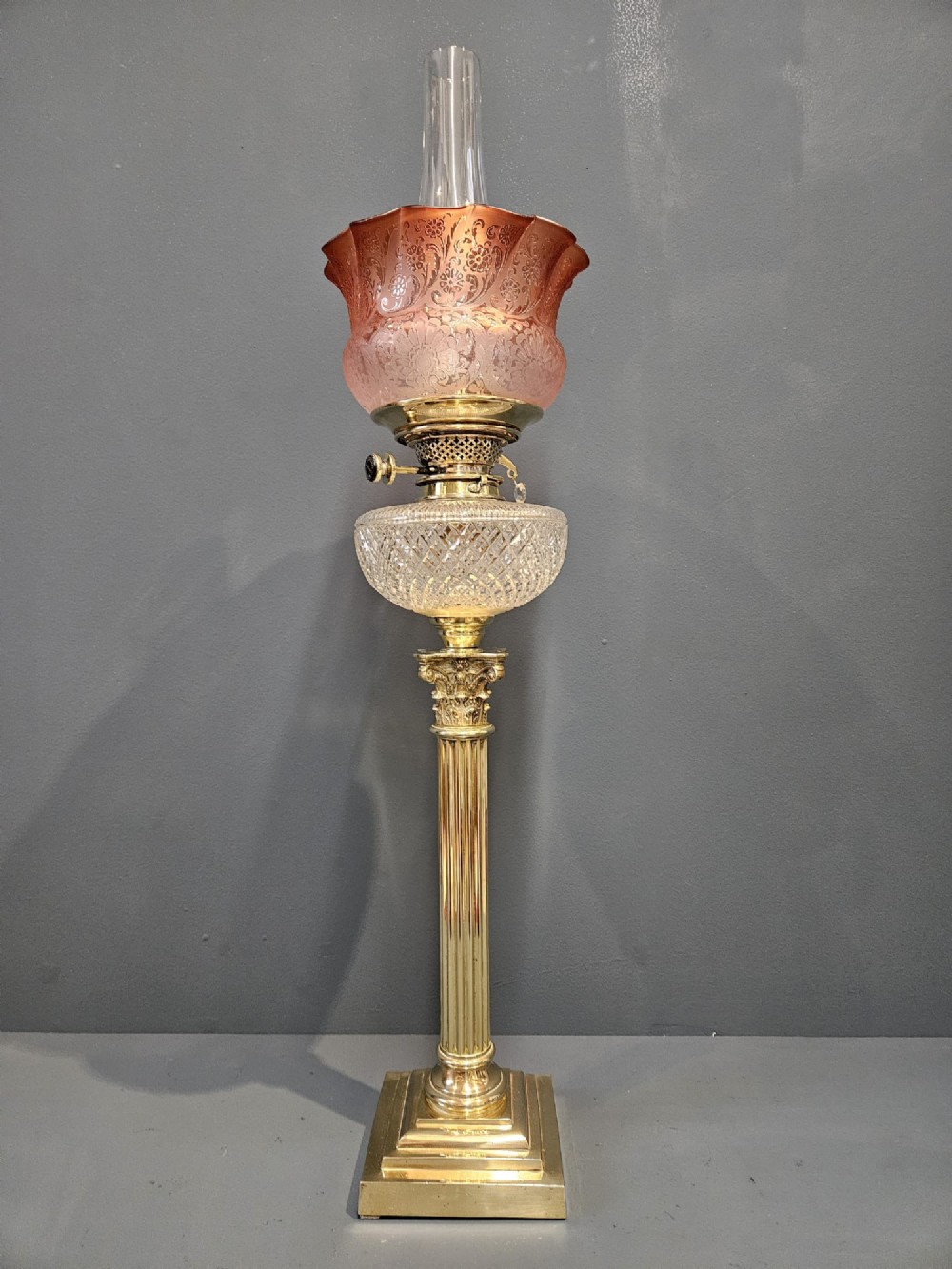 A Victorian oil lamp featuring a stepped brass base, fluted Corinthian column stem, cut crystal reservoir, etched pink glass shade, and clear glass chimney. View IV
