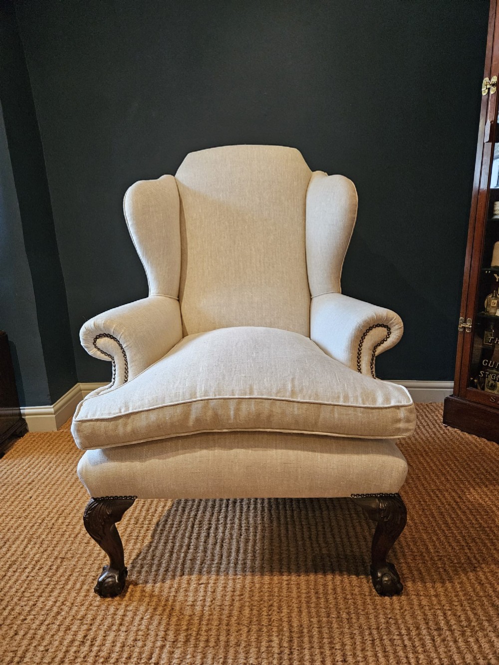 A pair of late Victorian wingback armchairs upholstered in natural oatmeal linen with dark carved cabriole legs and brass stud detailing. View V