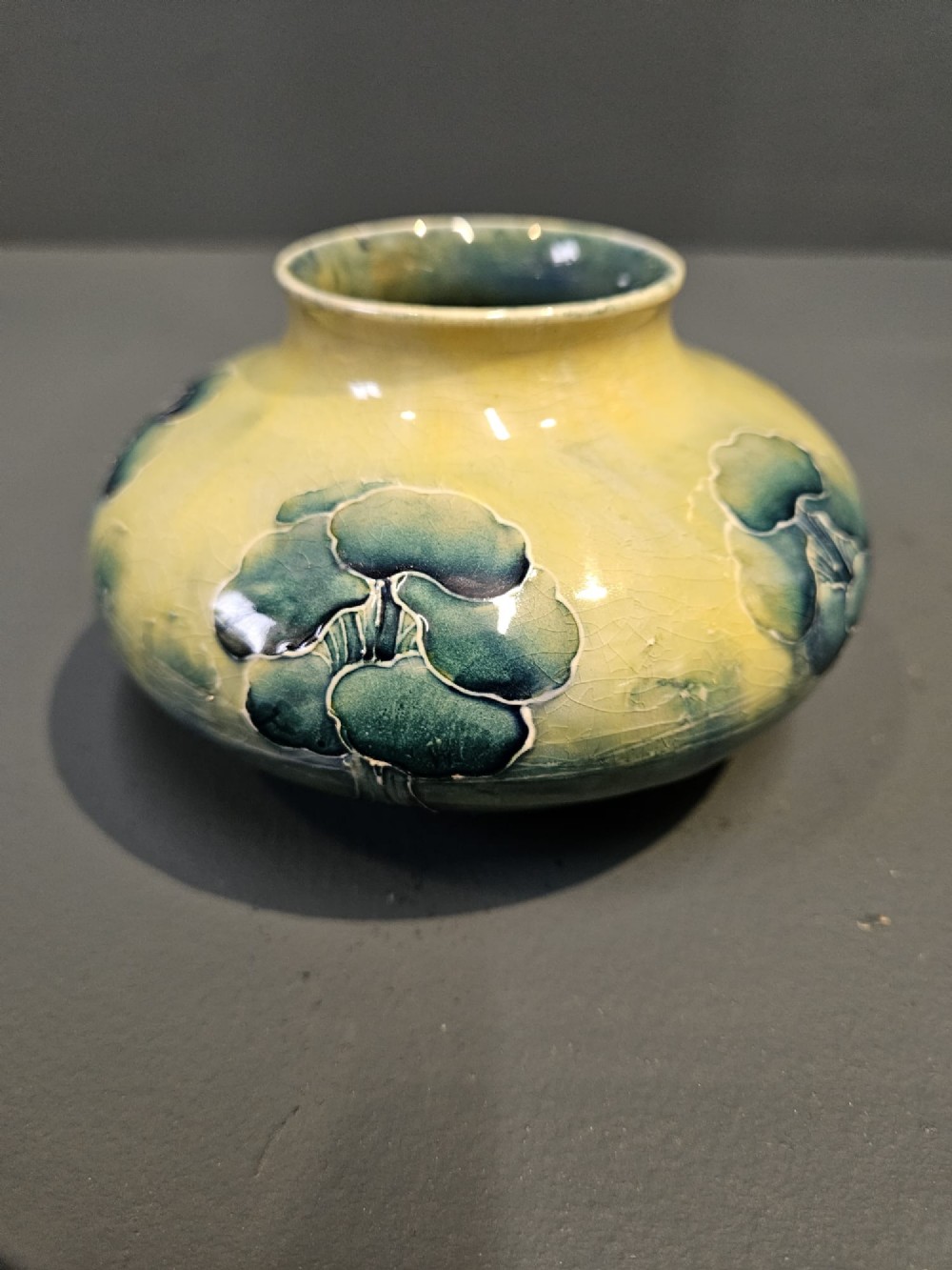 A squat ceramic Art Nouveau vase featuring a hand-painted tube-lined tree motif in shades of teal blue and green over a soft yellow background. View V
