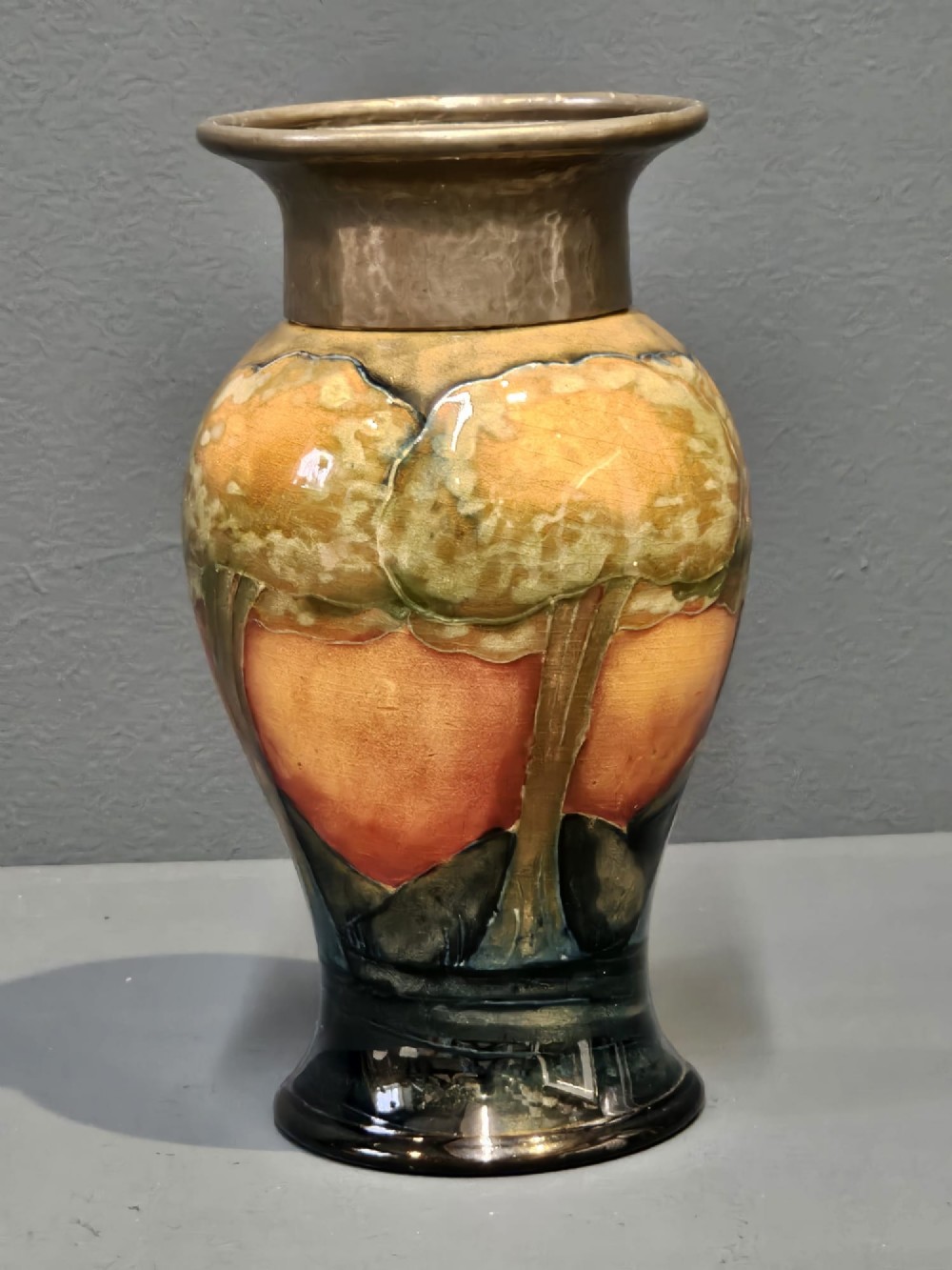 A Moorcroft Eventide glazed earthenware vase featuring a tubelined tree motif against an orange sky with a hammered pewter rim.