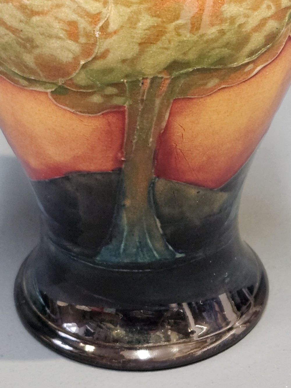 A Moorcroft Eventide glazed earthenware vase featuring a tubelined tree motif against an orange sky with a hammered pewter rim. View V