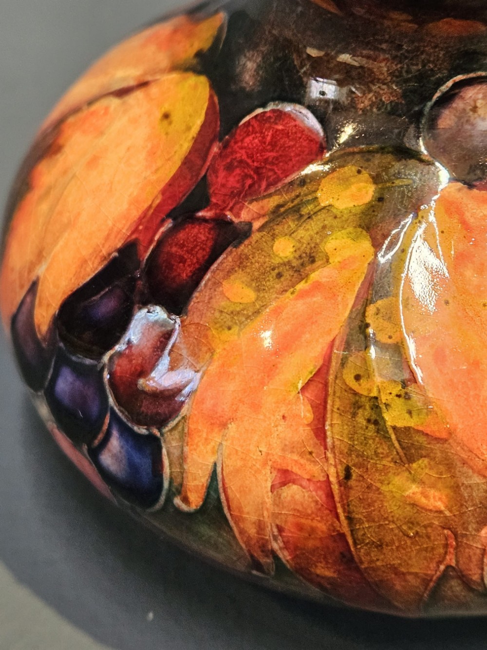 A small squat ceramic vase featuring tubelined leaf and berry motifs in shades of orange, yellow, and purple under a rich flambe glaze. View II