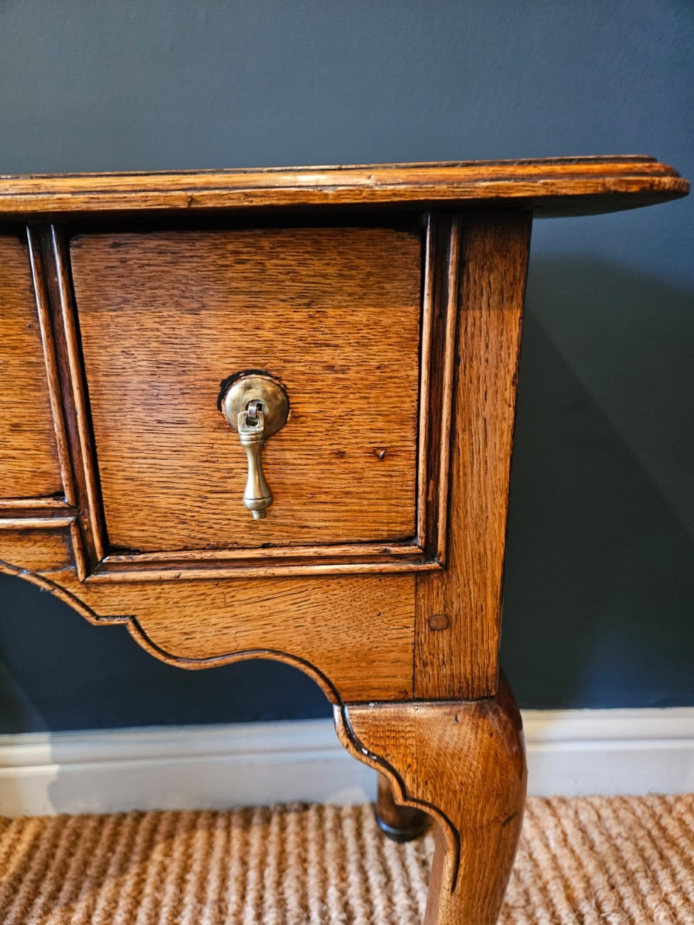 A small George II oak lowboy featuring three drawers with brass teardrop handles, a shaped apron, and cabriole legs terminating in pad feet. View II