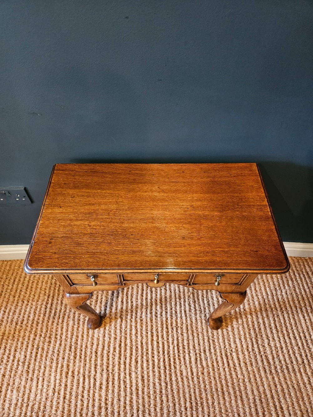 A small George II oak lowboy featuring three drawers with brass teardrop handles, a shaped apron, and cabriole legs terminating in pad feet. View III