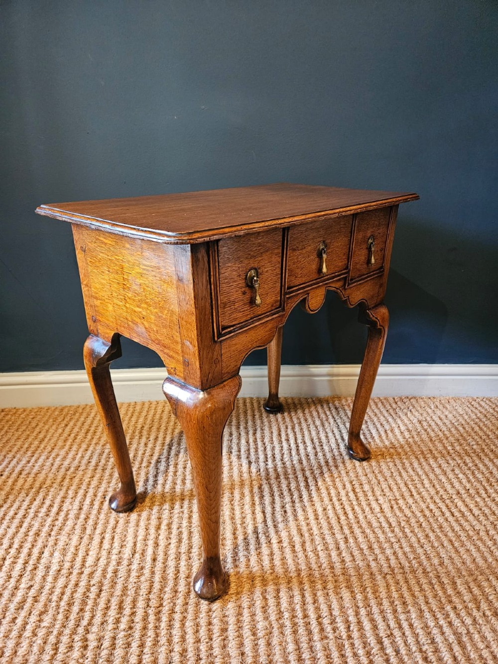 A small George II oak lowboy featuring three drawers with brass teardrop handles, a shaped apron, and cabriole legs terminating in pad feet. View IV