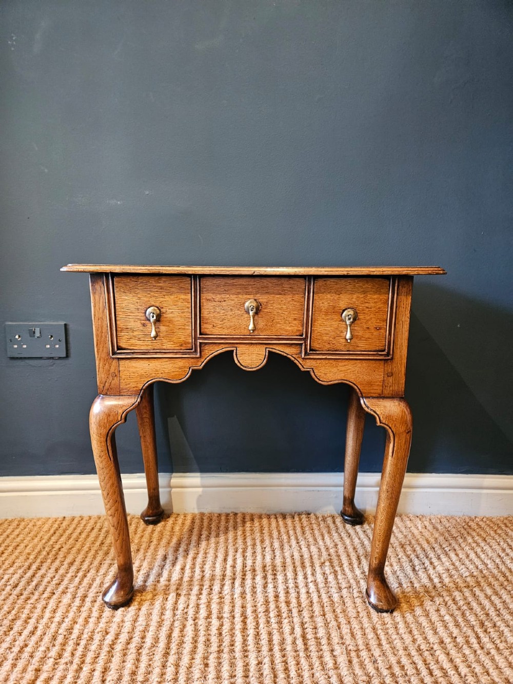 A small George II oak lowboy featuring three drawers with brass teardrop handles, a shaped apron, and cabriole legs terminating in pad feet. View V