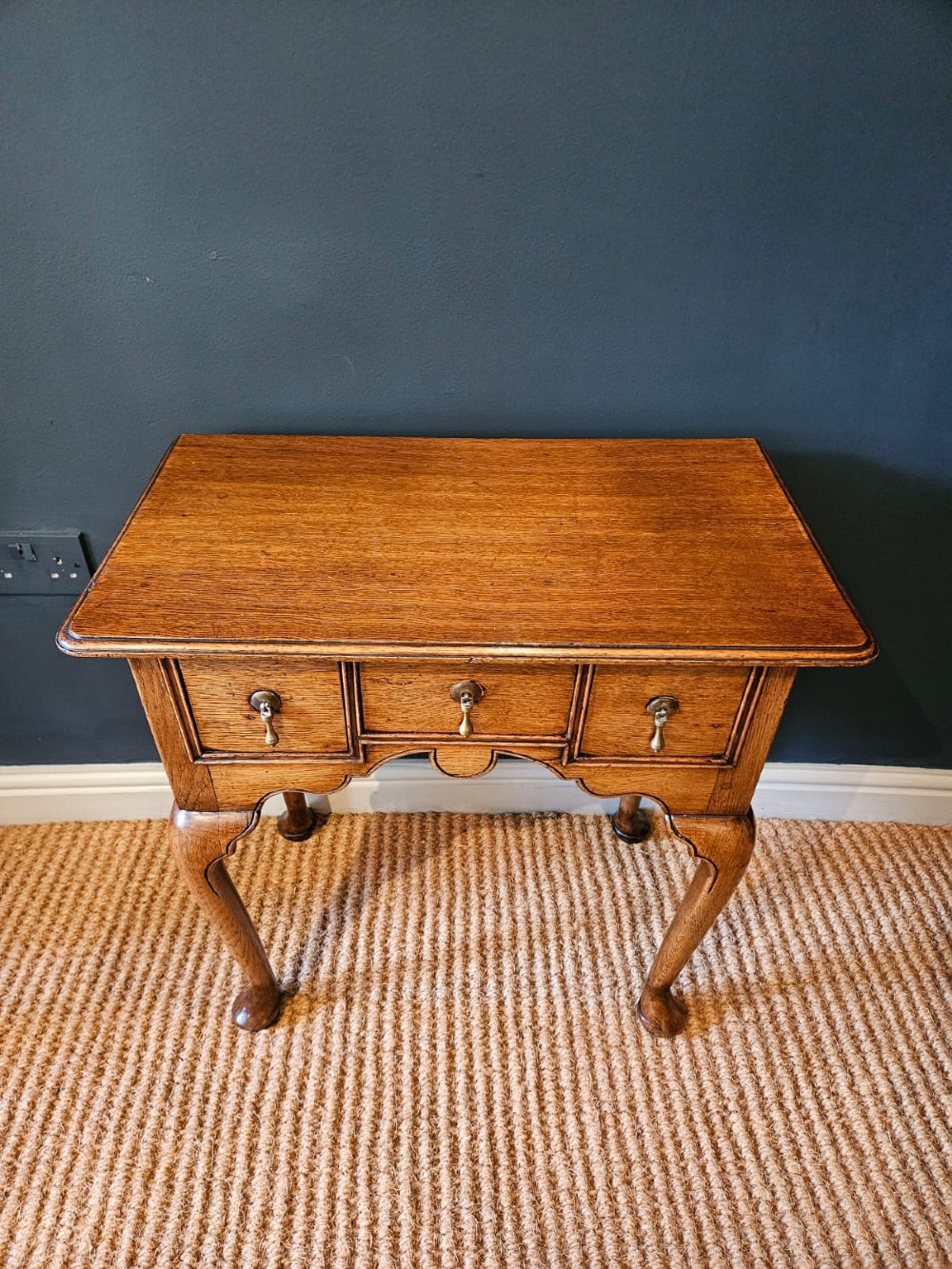 A small George II oak lowboy featuring three drawers with brass teardrop handles, a shaped apron, and cabriole legs terminating in pad feet. View VIII