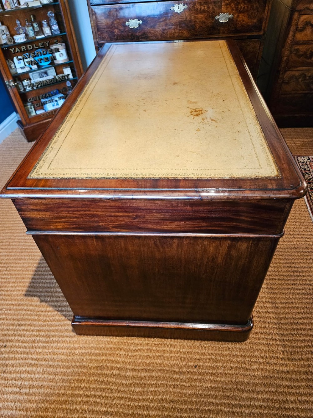 An antique Victorian mahogany pedestal desk with a tan leather writing surface, nine drawers fitted with brass handles, and solid plinth bases. View VI