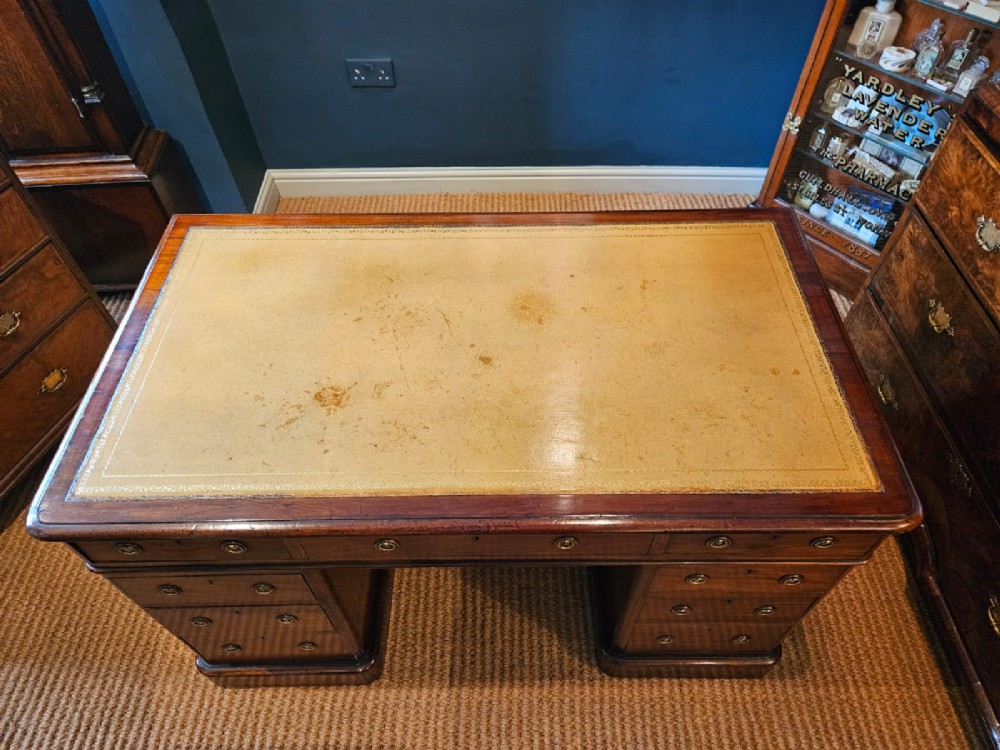 An antique Victorian mahogany pedestal desk with a tan leather writing surface, nine drawers fitted with brass handles, and solid plinth bases. View VII