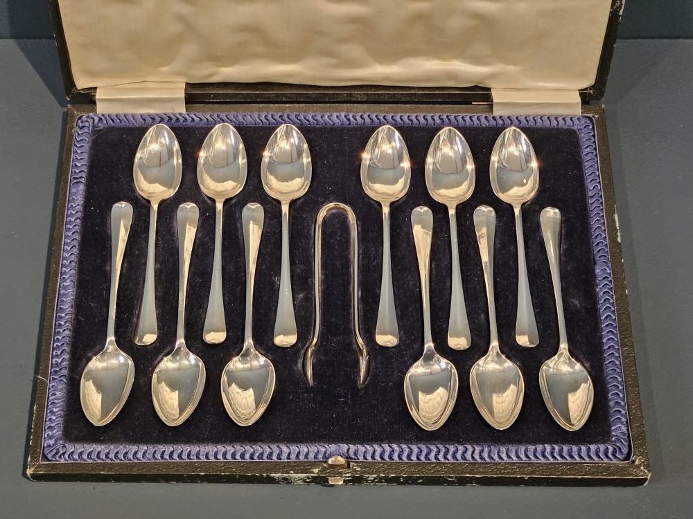 A cased set of twelve sterling silver teaspoons and matching sugar tongs displayed inside a dark blue velvet and cream satin lined box. View IX