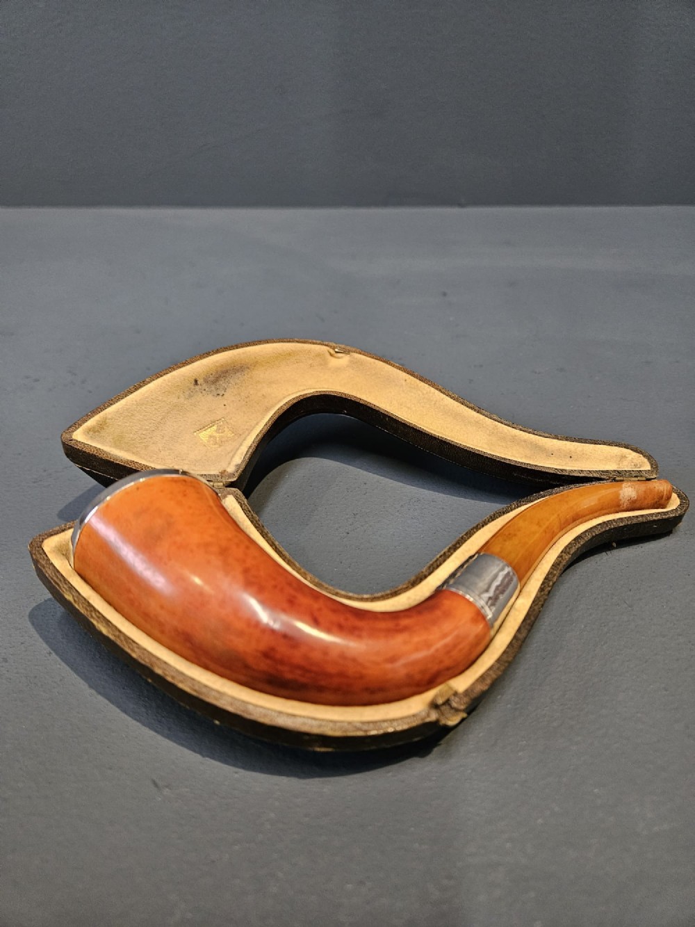 An Edwardian briar wood tobacco pipe featuring a silver band and amber stem resting inside its custom fitted presentation case.