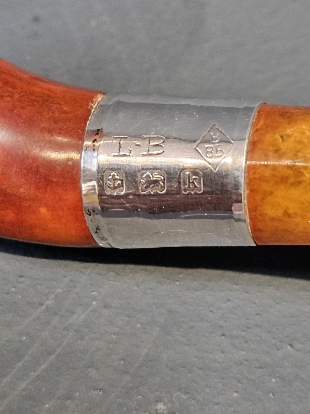 An Edwardian briar wood tobacco pipe featuring a silver band and amber stem resting inside its custom fitted presentation case. View II