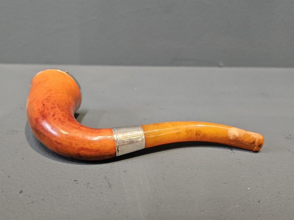 An Edwardian briar wood tobacco pipe featuring a silver band and amber stem resting inside its custom fitted presentation case. View III