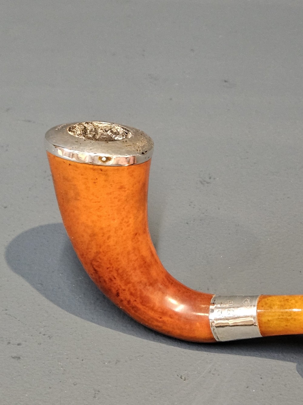 An Edwardian briar wood tobacco pipe featuring a silver band and amber stem resting inside its custom fitted presentation case. View VII