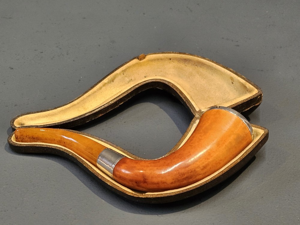 An Edwardian briar wood tobacco pipe featuring a silver band and amber stem resting inside its custom fitted presentation case. View VIII