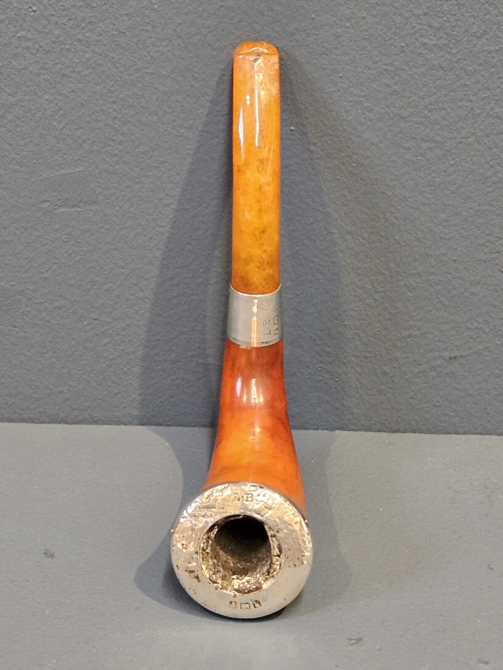 An Edwardian briar wood tobacco pipe featuring a silver band and amber stem resting inside its custom fitted presentation case. View IX