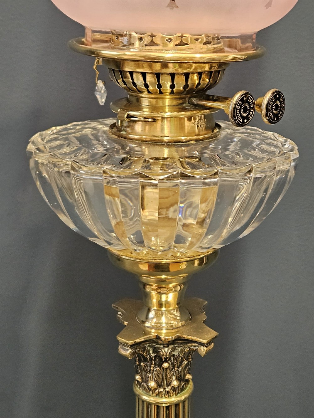 A Victorian brass oil lamp featuring a stepped square base, fluted Corinthian column, cut glass reservoir, and a flared etched cranberry glass shade. View IV