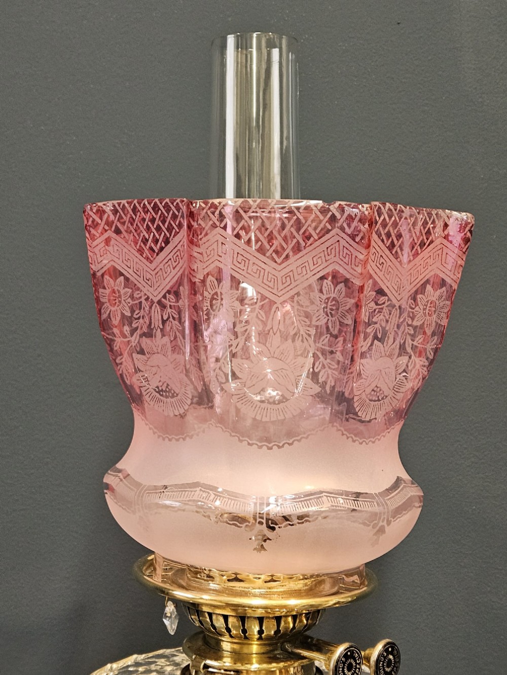 A Victorian brass oil lamp featuring a stepped square base, fluted Corinthian column, cut glass reservoir, and a flared etched cranberry glass shade. View V