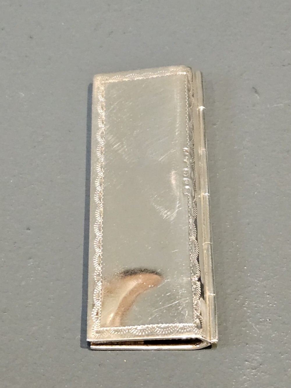 A slim rectangular silver box featuring intricate engraved foliate scrollwork and a central unengraved shield cartouche. View IV