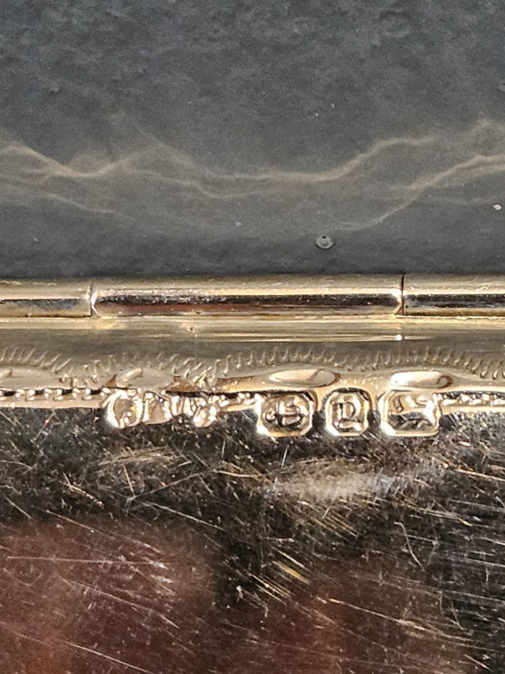 A slim rectangular silver box featuring intricate engraved foliate scrollwork and a central unengraved shield cartouche. View V