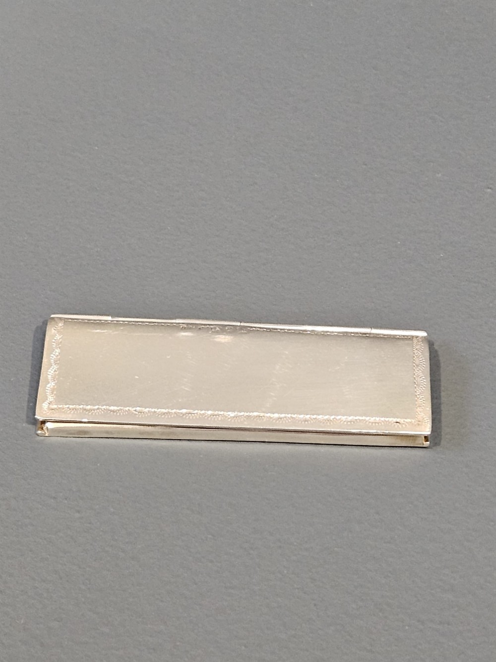 A slim rectangular silver box featuring intricate engraved foliate scrollwork and a central unengraved shield cartouche. View VIII