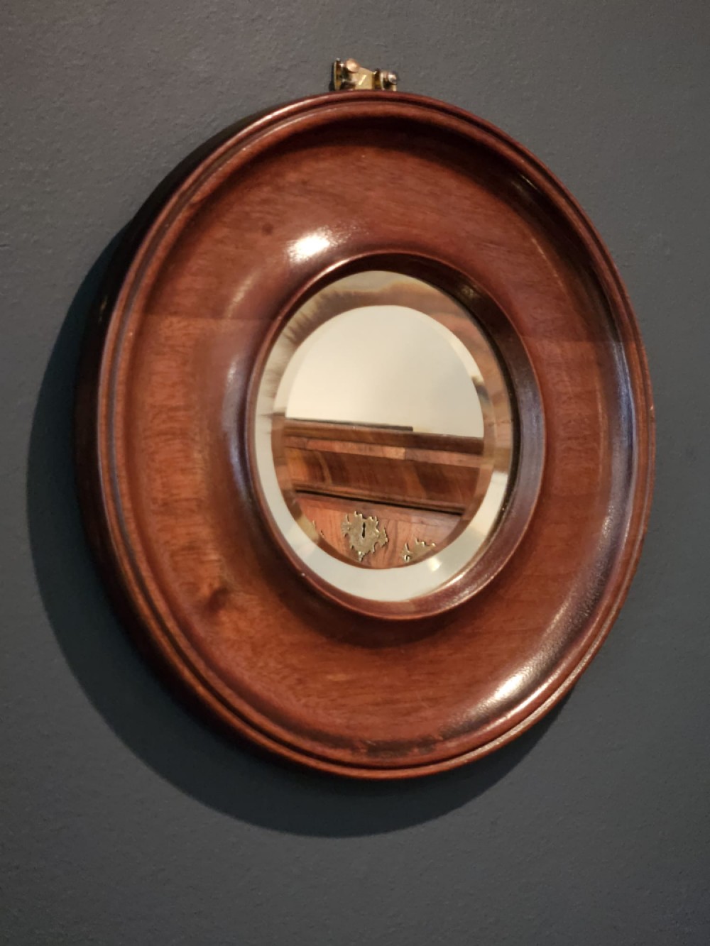 A small Victorian circular mirror featuring a turned mahogany frame with a central bevelled glass plate and top brass hanging loop. View VI