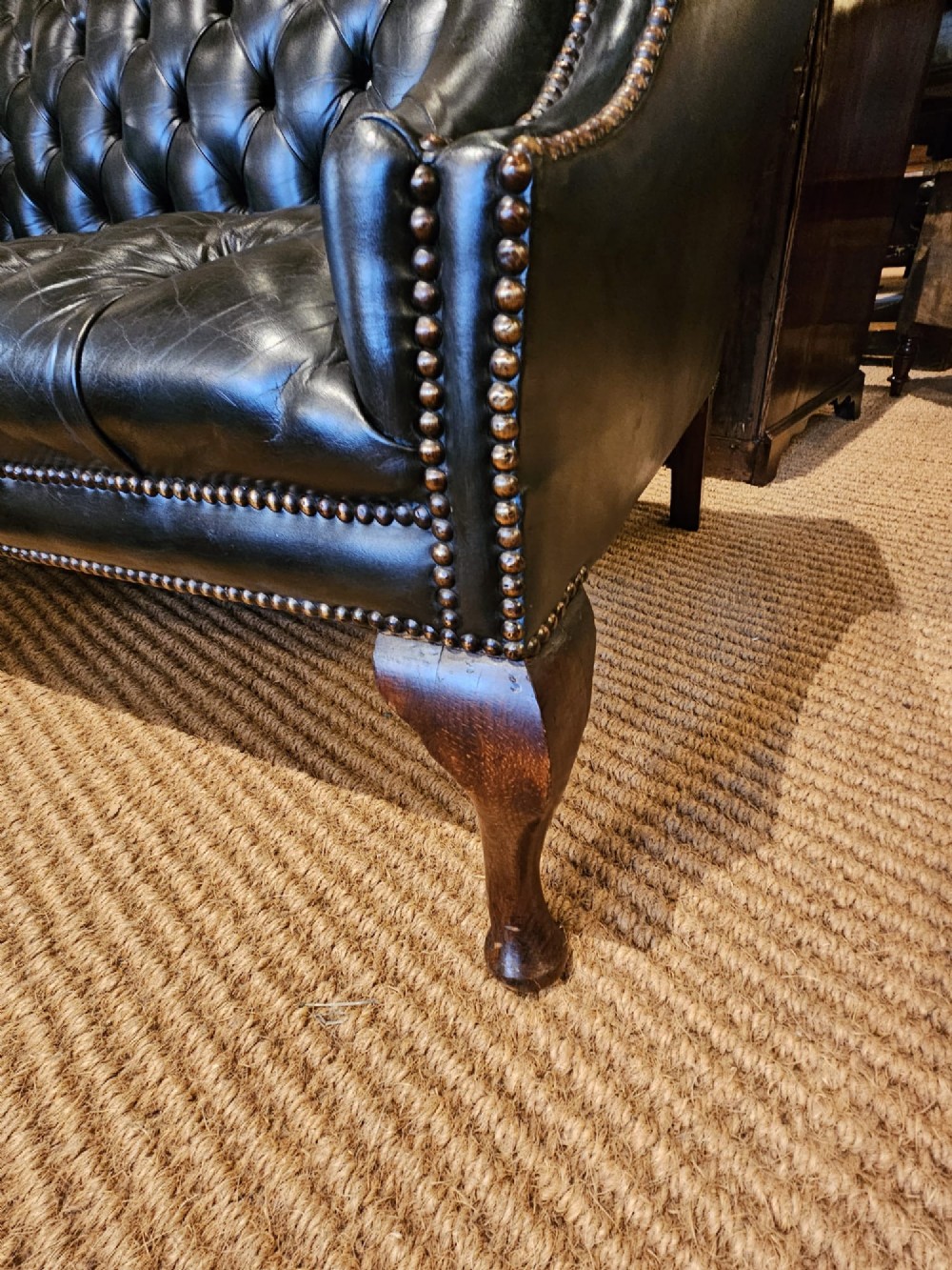 A small bottle green leather Chesterfield sofa featuring deep-buttoned tufting, brass studding along the scrolled arms, and dark wooden legs. View II