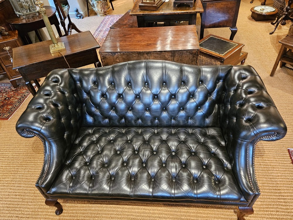 A small bottle green leather Chesterfield sofa featuring deep-buttoned tufting, brass studding along the scrolled arms, and dark wooden legs. View V