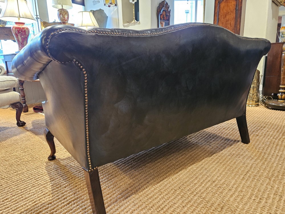 A small bottle green leather Chesterfield sofa featuring deep-buttoned tufting, brass studding along the scrolled arms, and dark wooden legs. View VI