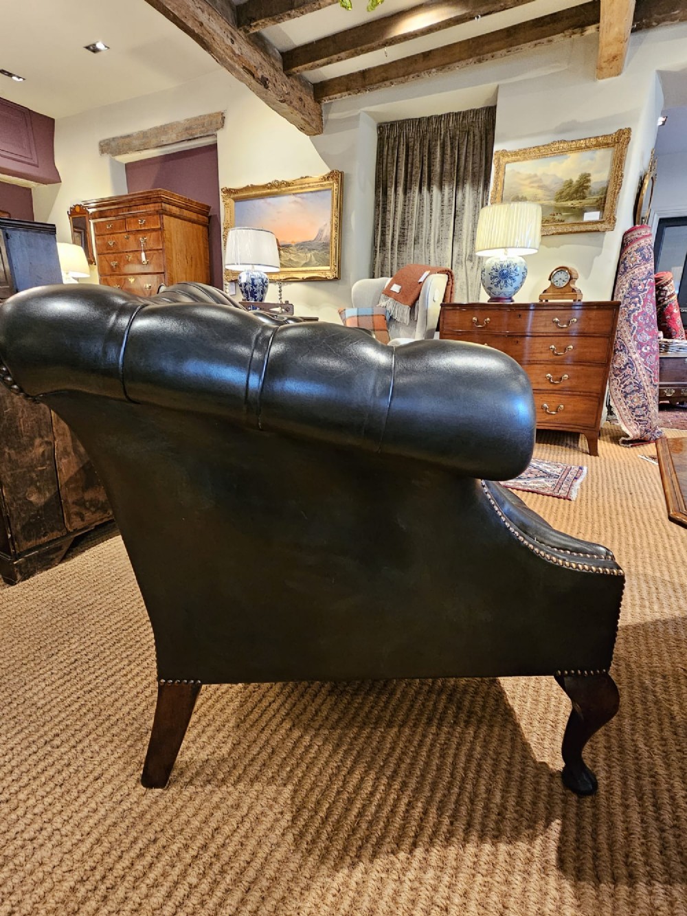 A small bottle green leather Chesterfield sofa featuring deep-buttoned tufting, brass studding along the scrolled arms, and dark wooden legs. View VII