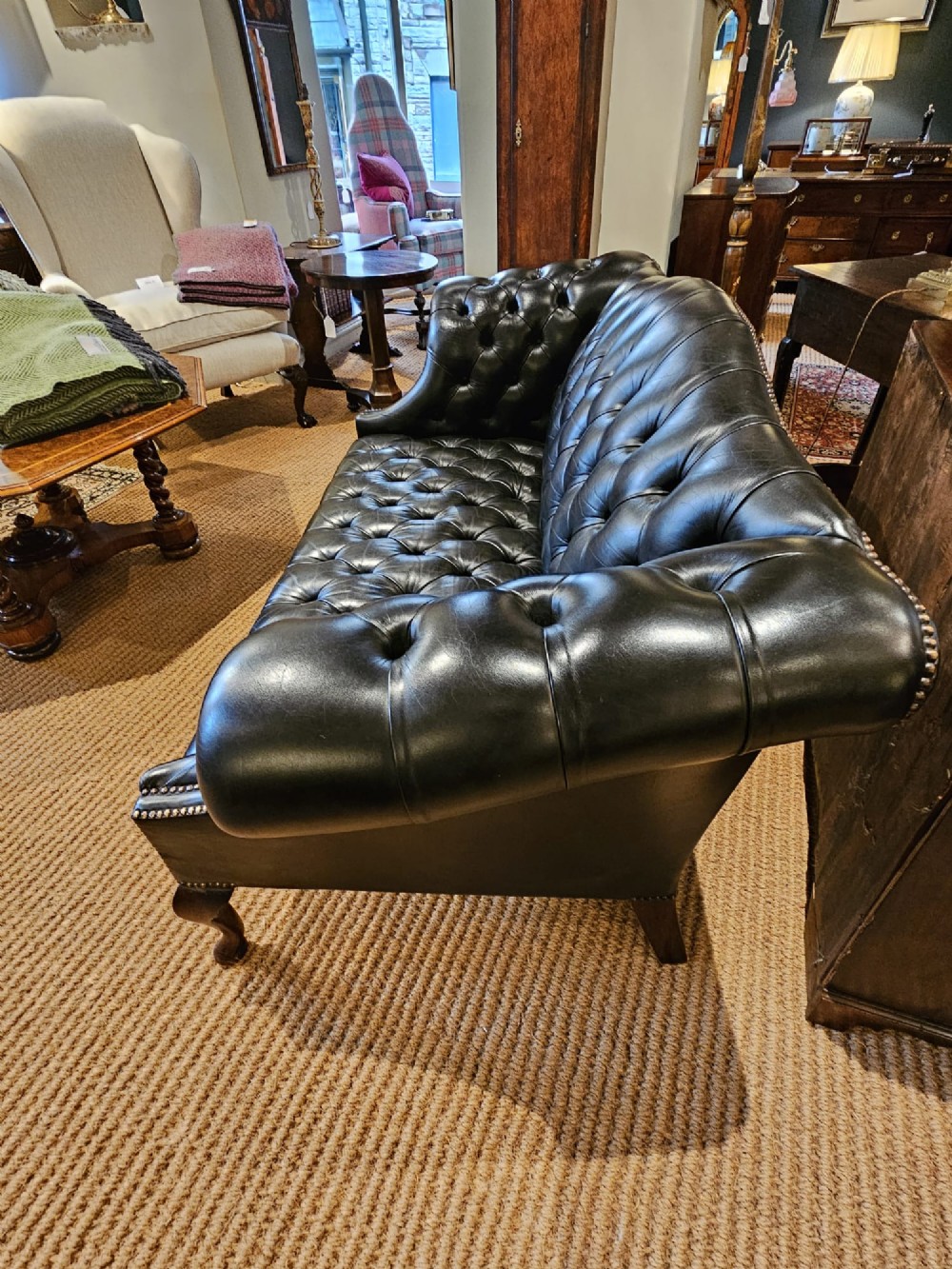 A small bottle green leather Chesterfield sofa featuring deep-buttoned tufting, brass studding along the scrolled arms, and dark wooden legs. View IX