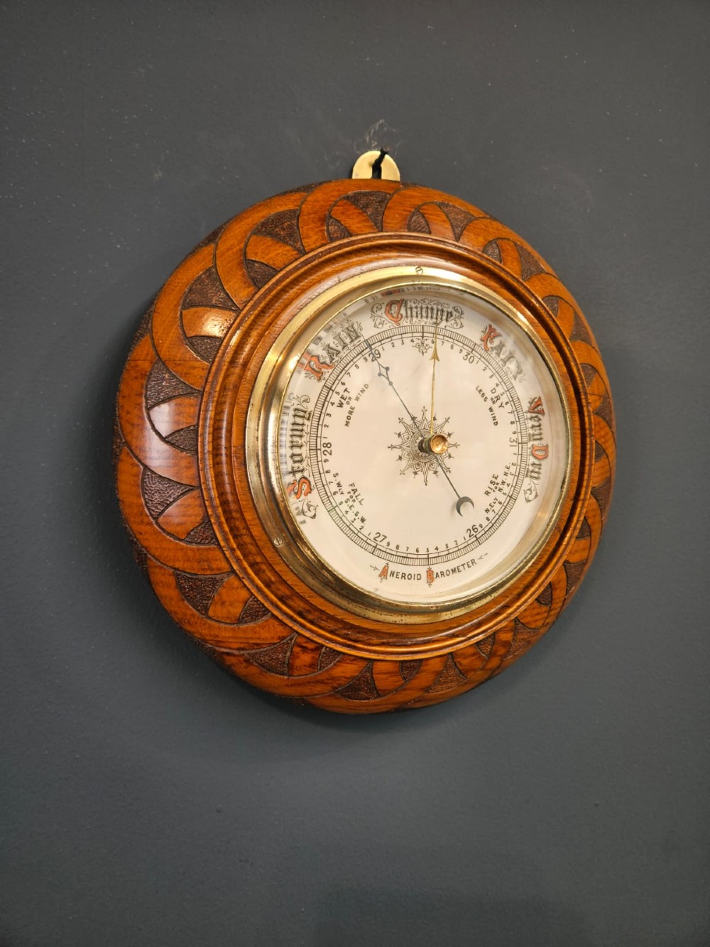 A circular Victorian aneroid wall barometer housed in a turned and carved oak case with a brass bezel. View V
