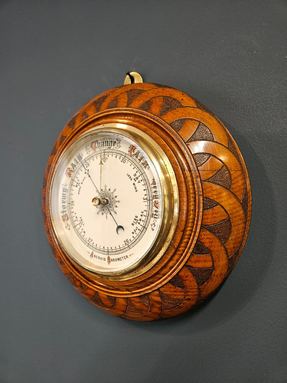 A circular Victorian aneroid wall barometer housed in a turned and carved oak case with a brass bezel. View VI