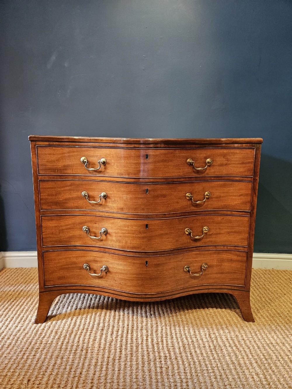 A George III mahogany chest of drawers featuring a curved serpentine front, four graduated drawers with brass swan-neck handles, and splayed feet.