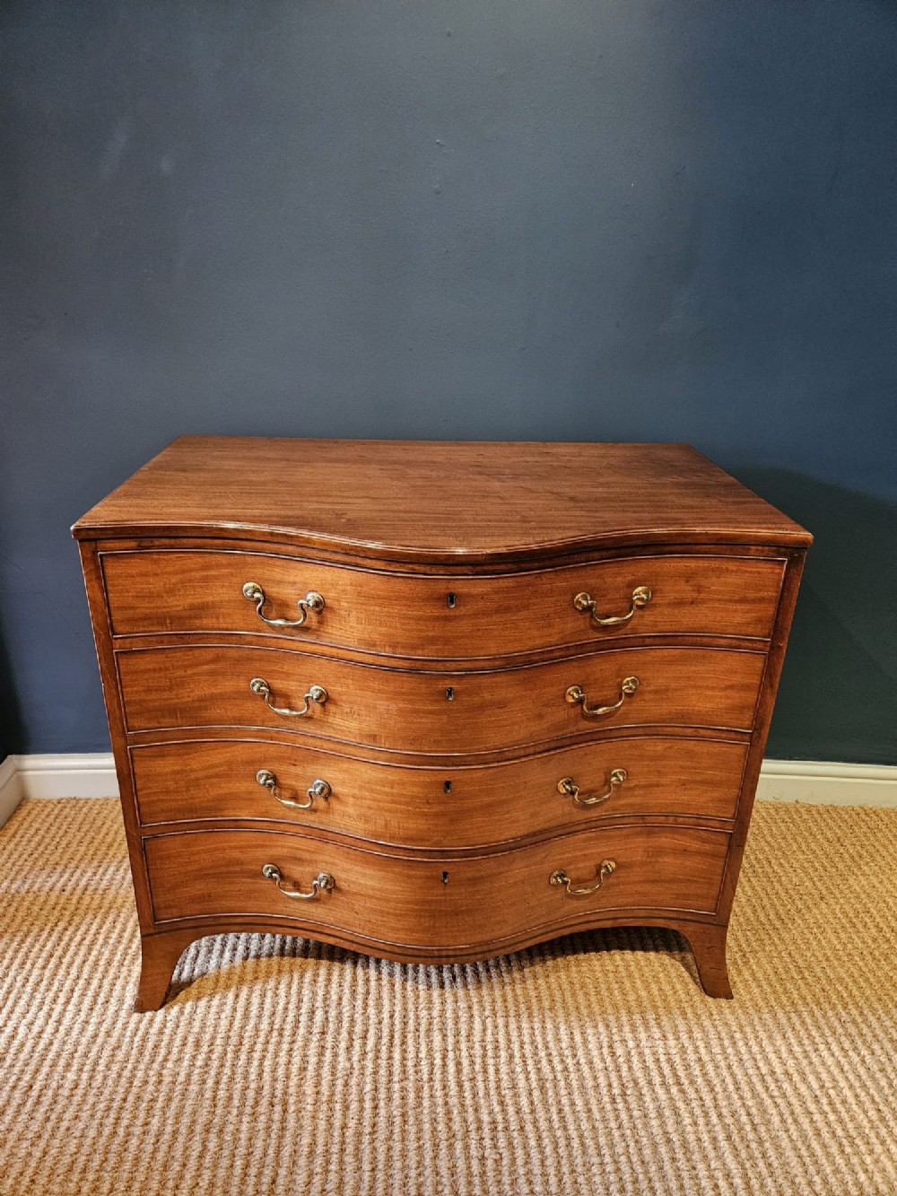 A George III mahogany chest of drawers featuring a curved serpentine front, four graduated drawers with brass swan-neck handles, and splayed feet. View III