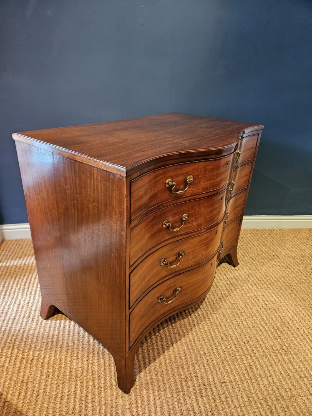 A George III mahogany chest of drawers featuring a curved serpentine front, four graduated drawers with brass swan-neck handles, and splayed feet. View V