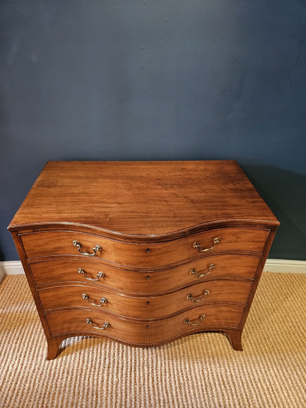 A George III mahogany chest of drawers featuring a curved serpentine front, four graduated drawers with brass swan-neck handles, and splayed feet. View VIII