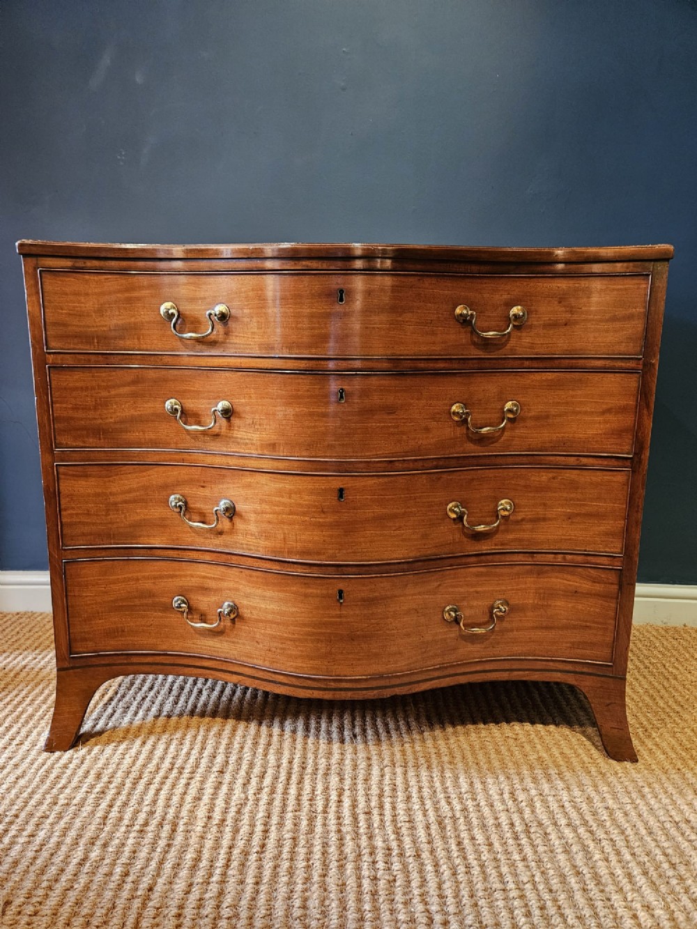 A George III mahogany chest of drawers featuring a curved serpentine front, four graduated drawers with brass swan-neck handles, and splayed feet. View IX