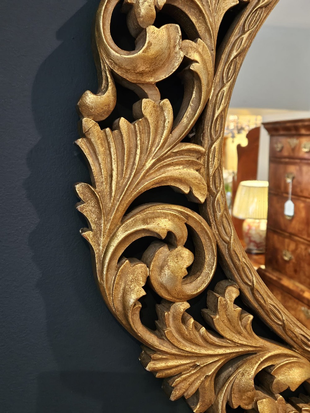 An ornate oval wall mirror featuring a heavily carved timber frame with gold gilt finish, decorated with openwork acanthus leaf scrolls and a top cresting. View III