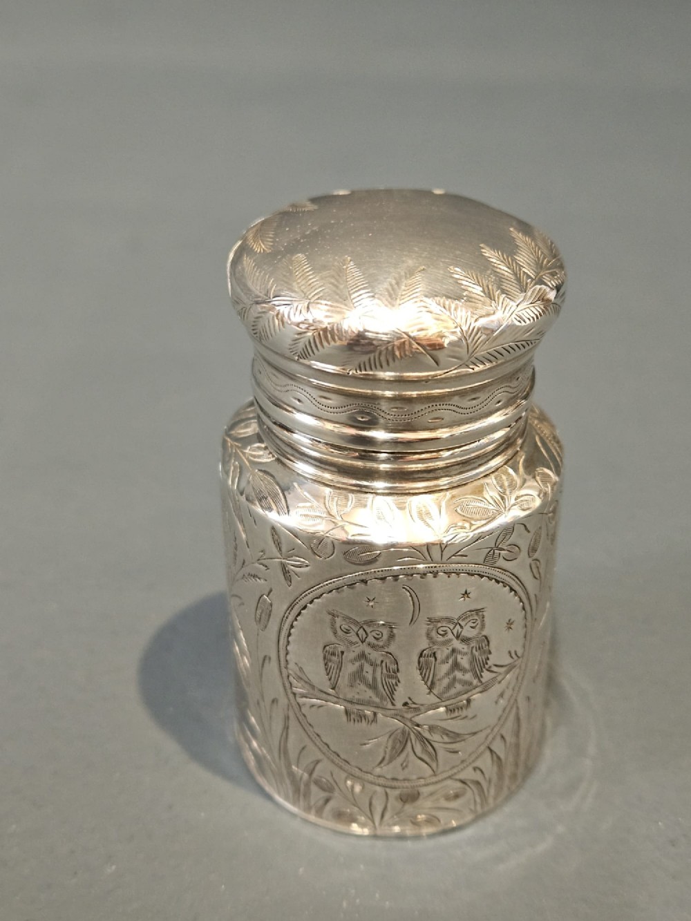 A cylindrical Victorian silver scent bottle featuring engraved artwork of two owls perched on a branch within a circular border. View II