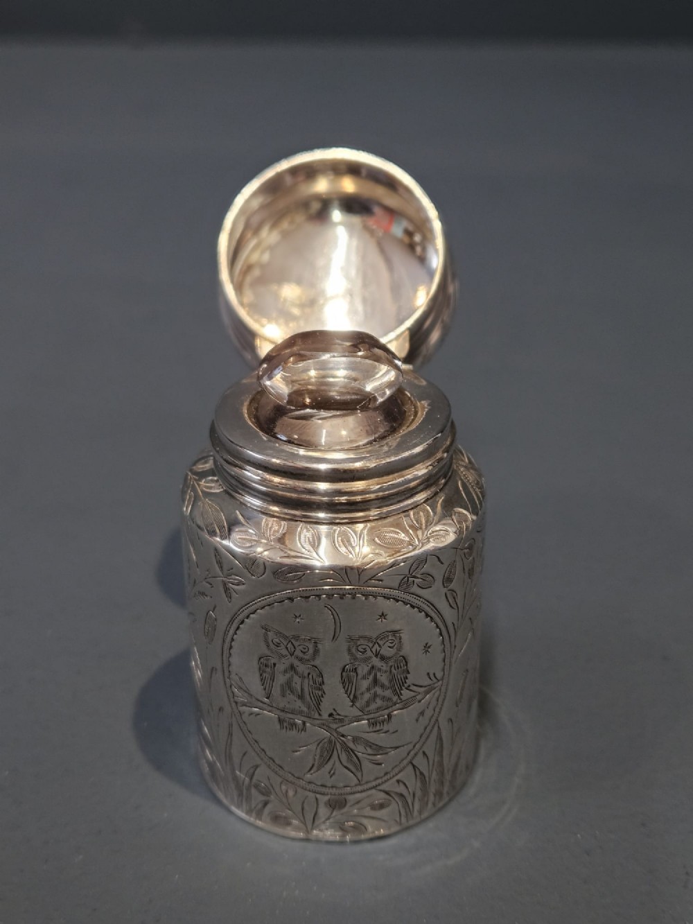 A cylindrical Victorian silver scent bottle featuring engraved artwork of two owls perched on a branch within a circular border. View IV