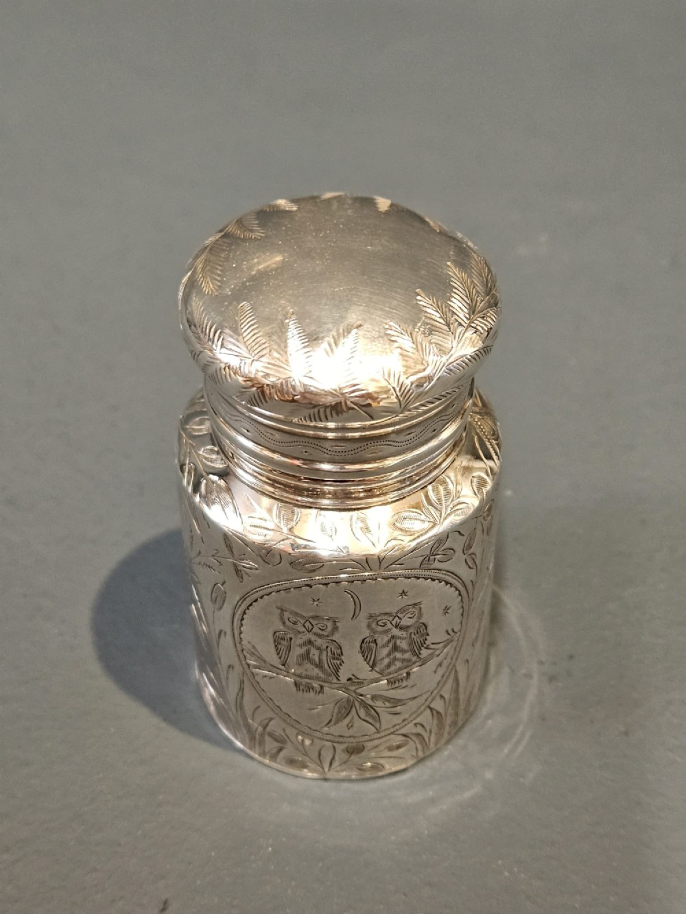 A cylindrical Victorian silver scent bottle featuring engraved artwork of two owls perched on a branch within a circular border. View VI