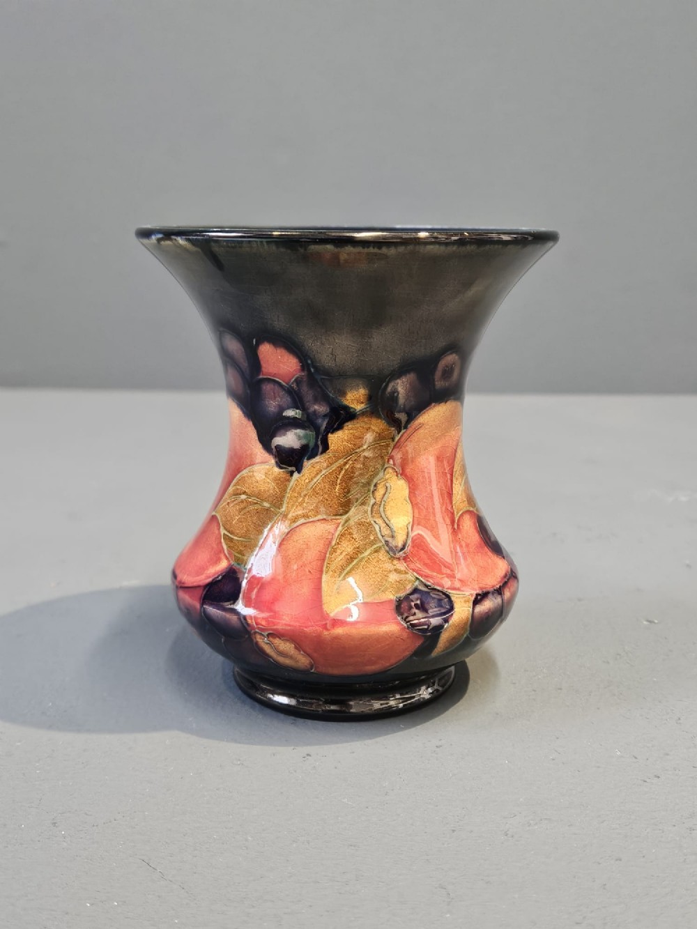 An Art Nouveau Moorcroft earthenware vase with a flared rim, featuring hand-painted tube-lined pomegranates and berries against a deep cobalt blue background. View III