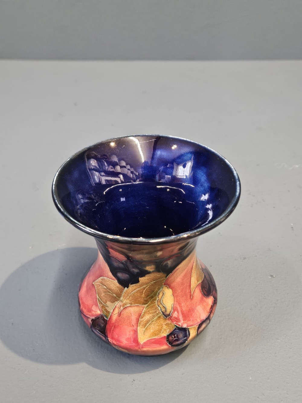 An Art Nouveau Moorcroft earthenware vase with a flared rim, featuring hand-painted tube-lined pomegranates and berries against a deep cobalt blue background. View IV