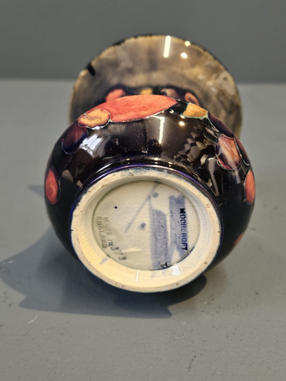 An Art Nouveau Moorcroft earthenware vase with a flared rim, featuring hand-painted tube-lined pomegranates and berries against a deep cobalt blue background. View V