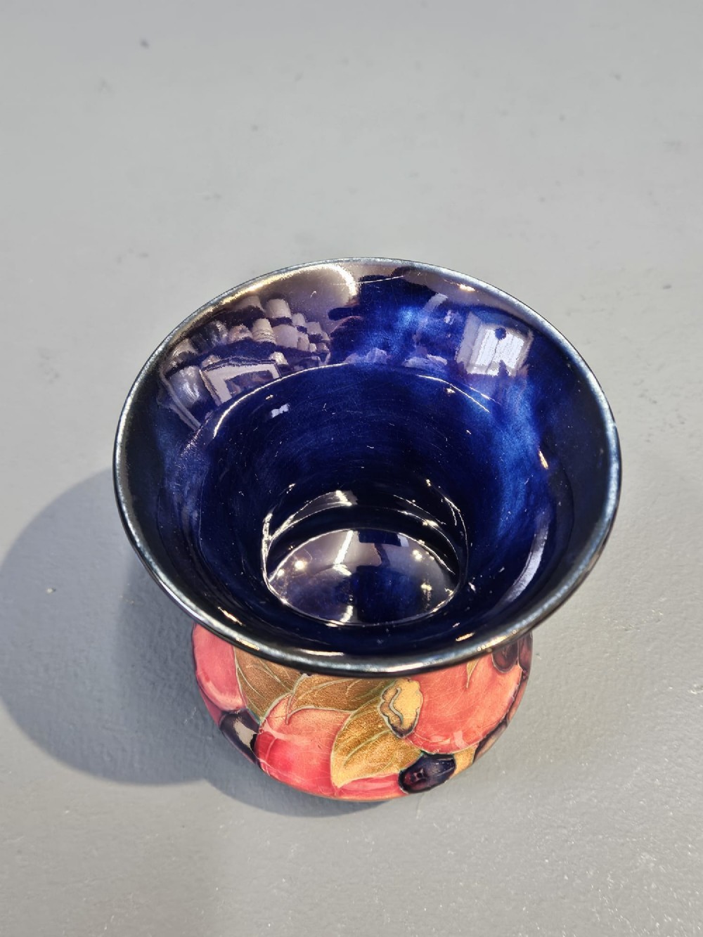 An Art Nouveau Moorcroft earthenware vase with a flared rim, featuring hand-painted tube-lined pomegranates and berries against a deep cobalt blue background. View VI