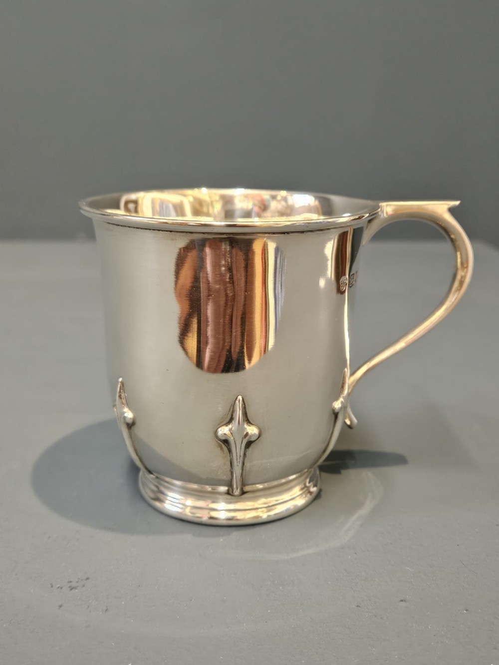 A hallmarked sterling silver mug with raised strapwork details around the lower body, a gilded interior, and a single loop handle. View II