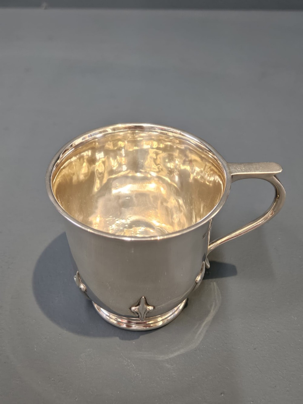 A hallmarked sterling silver mug with raised strapwork details around the lower body, a gilded interior, and a single loop handle. View VI